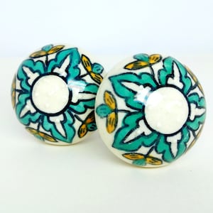 以下が含まれることがあります： 白い背景に緑と黄色の花柄が描かれたセラミック製のノブが2つ