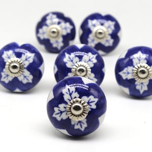 Puede incluir: Juego de seis pomos de armario de cerámica azul y blanca con un diseño floral. Cada pomo presenta una flor blanca con un centro plateado.