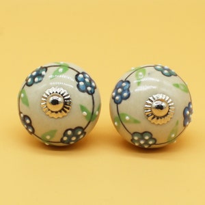 Peut inclure: Deux boutons en céramique avec un motif floral. Les boutons sont blancs avec des fleurs bleues et vertes et ont un centre argenté.