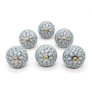 May include: Set of six gray ceramic cabinet knobs with a floral design. Each knob has a silver base and a gold center.