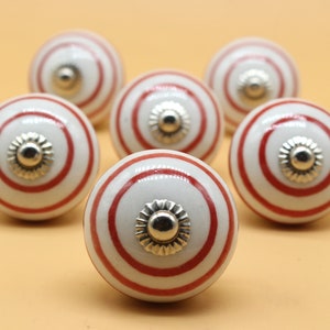 以下が含まれることがあります： 赤と銀のアクセントが付いた白いセラミック製のキャビネットノブ6個セット。