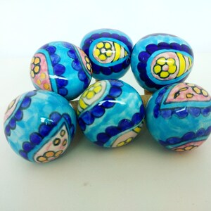 May include: Six blue ceramic ornaments with a white background and colorful floral designs. The ornaments are round and have a glossy finish.