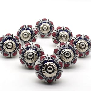 Pode incluir: Dez botões de cerâmica para gavetas com fundo branco e design floral em tons de azul e rosa. Cada botão tem um centro de metal prateado.
