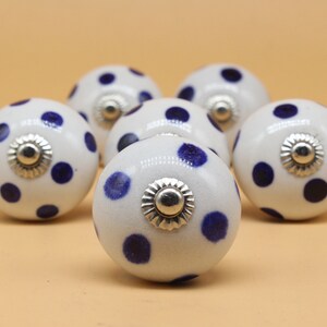 May include: Six white ceramic cabinet knobs with blue polka dots and silver accents.