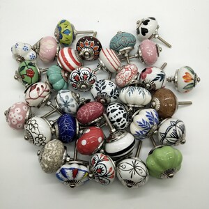 May include: A collection of colourful ceramic cabinet knobs with various patterns and designs. The knobs are white with different coloured accents and patterns, including red, blue, green, and yellow.