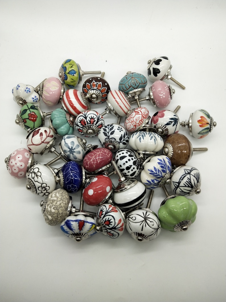 May include: A collection of colourful ceramic cabinet knobs with various patterns and designs. The knobs are white with different coloured accents and patterns, including red, blue, green, and yellow.