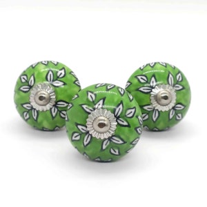 Può includere: Tre pomelli in ceramica verde con motivi floreali bianchi e dettagli argentati. I pomelli sono rotondi e hanno un centro rialzato.