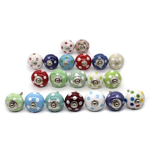 Op de afbeelding: Een verzameling van 18 keramische kastknoppen met een stippenpatroon in verschillende kleuren, waaronder rood, blauw, groen, wit en roze. De knoppen hebben een zilveren metalen basis.