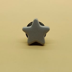 Puede incluir: Un pomo de cerámica en forma de estrella de color gris claro con una base negra.