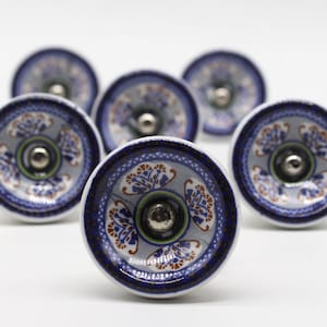 Könnte beinhalten: Sechs blaue und weiße Keramikknöpfe mit floralem Design und silbernen Akzenten. Die Knöpfe sind rund und haben einen erhöhten Rand.