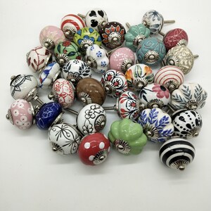 May include: A collection of colourful ceramic cabinet knobs with various floral, geometric, and abstract designs. The knobs have a silver metal base and are perfect for adding a touch of whimsy to any home decor.
