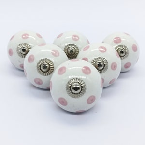 Op de afbeelding: Zes witte keramische knoppen met roze stippen en zilveren accenten.