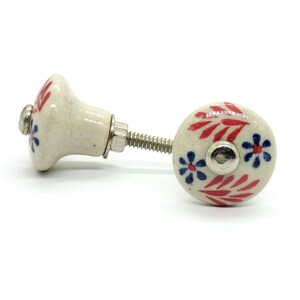 May include: White ceramic knob with red and blue floral design. The knob has a silver screw.