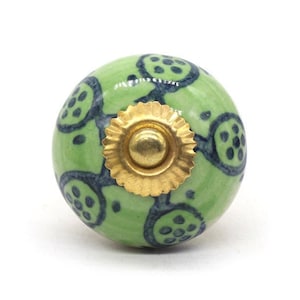 Könnte beinhalten: Grüner Keramik-Knopf mit goldfarbenem Metallakzent und einem blauen und weißen Muster.