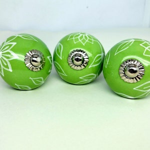 May include: Three green ceramic cabinet knobs with white floral designs and silver accents.