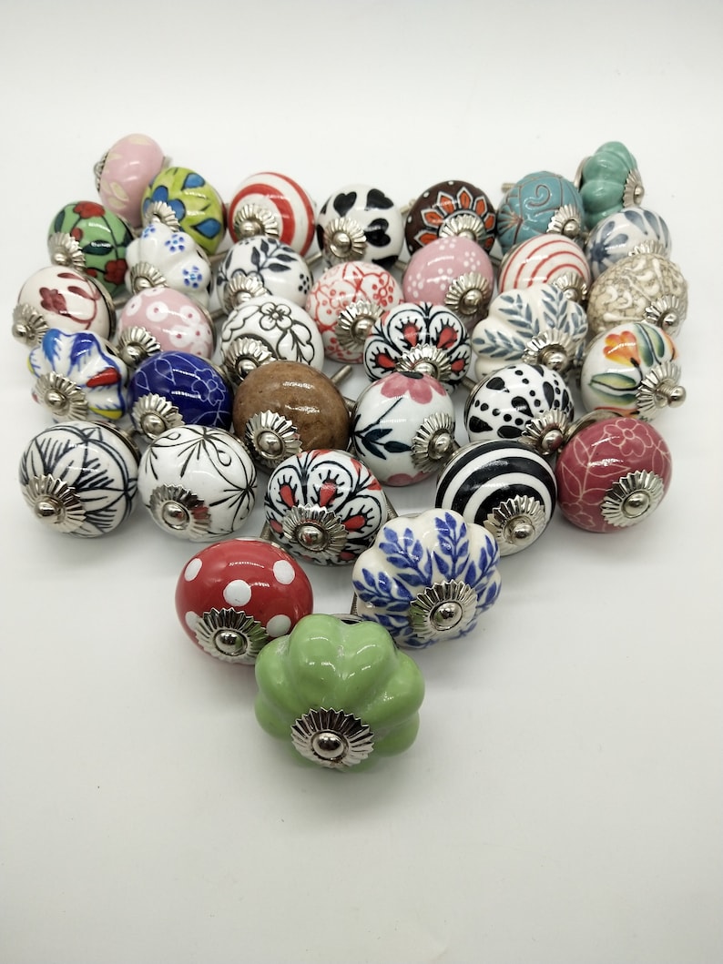May include: A collection of 25 ceramic cabinet knobs with various colourful patterns and designs. The knobs are round and have a silver metal base.