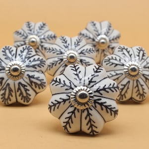 May include: Six white ceramic cabinet knobs with a black floral design and silver accents.