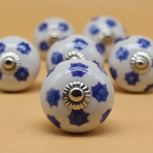 May include: Six white ceramic knobs with blue floral designs and silver accents. The knobs are round and have a smooth finish.