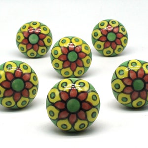 Könnte beinhalten: Sechs Keramik-Schrankknöpfe mit Blumenmuster. Die Knöpfe sind gelb, grün und rot mit schwarzem Umriss.