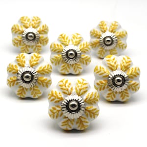 May include: Six white ceramic cabinet knobs with a yellow floral design and silver accents.