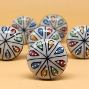 May include: Six white ceramic cabinet knobs with a colorful teardrop design. The knobs have a black outline and white dots in the center of each teardrop.
