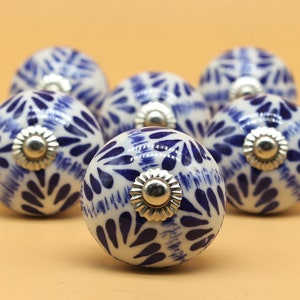Könnte beinhalten: Sechs weiße Keramik-Schrankknöpfe mit einem blauen und weißen Blumenmuster. Die Knöpfe haben eine silberne Metallbasis.