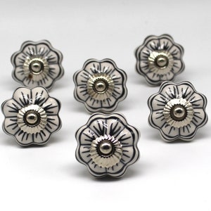 May include: Six white ceramic drawer knobs with a black floral design and silver accents.