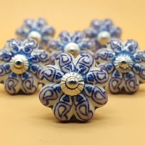 May include: Six white ceramic cabinet knobs with a blue and purple paisley pattern and silver accents.
