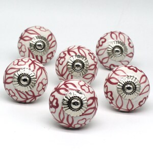 May include: Six white ceramic cabinet knobs with a red floral design and silver accents.