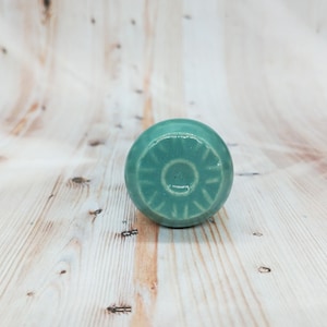May include: A teal blue ceramic knob with a circular design. The knob has a raised center circle and radiating lines.