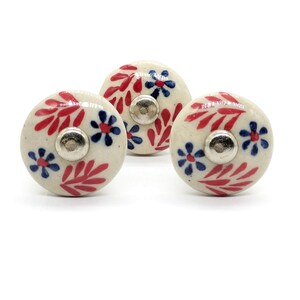 May include: Three white ceramic knobs with red and blue floral designs. The knobs have a silver metal base.