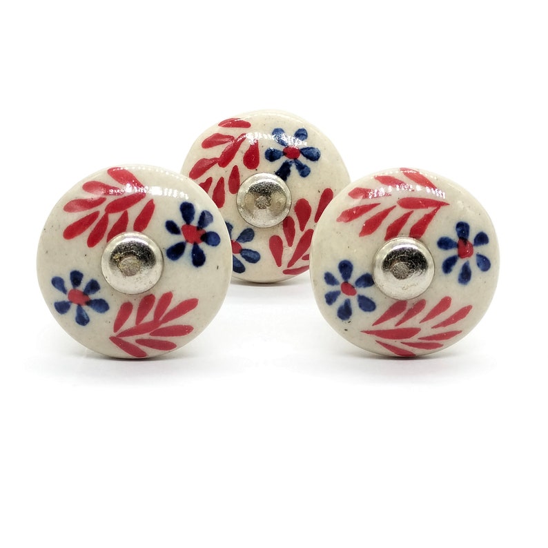 May include: Three white ceramic knobs with red and blue floral designs. The knobs have a silver metal base.