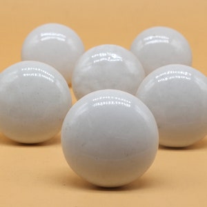 May include: Six white ceramic knobs with a smooth, glossy finish. The knobs are round and have a slight variation in texture.