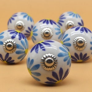 May include: Set of six ceramic knobs with a white background and blue and yellow floral pattern. The knobs have a silver metal base.