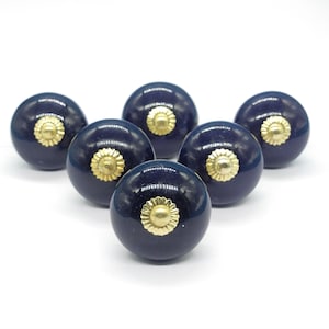 Könnte beinhalten: Sechs dunkelblaue Keramik-Schrankknöpfe mit goldenen Akzenten. Jeder Knopf hat eine runde Form mit einer erhabenen, dekorativen goldenen Mitte.
