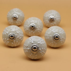 May include: Six off-white ceramic cabinet knobs with a white floral design and silver metal accents.