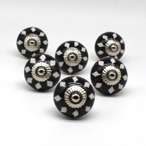 May include: Six black and white ceramic knobs with a silver center. The knobs have a diamond pattern.