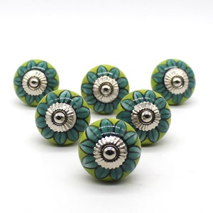 Può includere: Sei pomelli rotondi per armadietti con una base verde lime e un motivo a petali di fiori verde acqua scuro che si irradia dal centro. Ogni pomello presenta un elemento in metallo color argento al centro con un bordo scanalato e liscio.