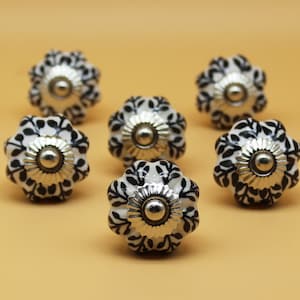 May include: Seven black and white ceramic cabinet knobs with a floral design and silver accents.
