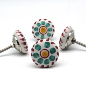 May include: Four white ceramic cabinet knobs with a green and red floral design. The knobs have a silver screw for attaching to a cabinet door.