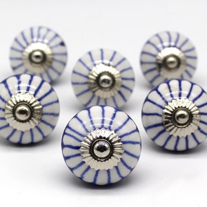 Könnte beinhalten: Sechs weiße Keramik-Schrankknöpfe mit blauen Streifen und silbernen Akzenten. Die Knöpfe haben eine abgerundete Form und ein erhabenes Design.