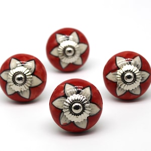 May include: Four red ceramic drawer knobs with white flower designs and silver centers.