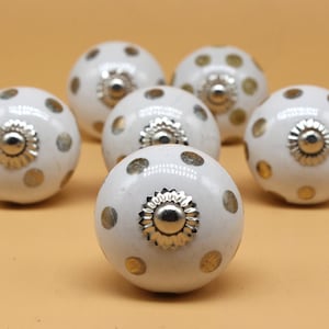 May include: Six white ceramic cabinet knobs with gold polka dots and silver accents.