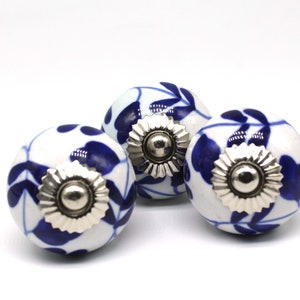May include: Three white ceramic cabinet knobs with blue floral designs and silver accents.