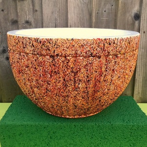 May include: A large, white ceramic planter with a speckled orange and brown glaze. The planter is sitting on a green block.