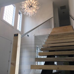 May include: A modern staircase with wooden steps and a glass railing. A white chandelier hangs from the ceiling above the staircase.