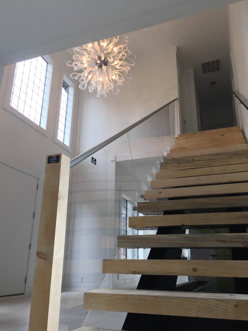 May include: A modern staircase with wooden steps and a glass railing. A white chandelier hangs from the ceiling above the staircase.