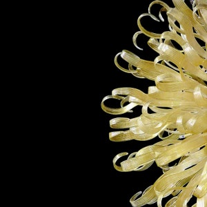 May include: A gold-colored glass sculpture with a delicate, floral design. The sculpture is made up of many thin, twisted strands of glass that create a flowing, organic shape.