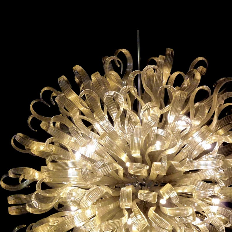 May include: A large, gold-colored chandelier made of many glass ribbons. The chandelier is lit with small, white lights.