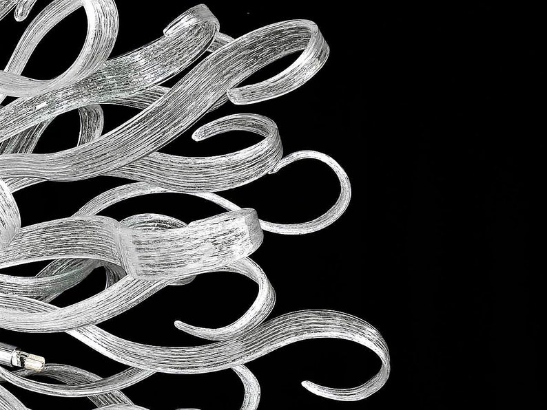 May include: A silver chandelier with a unique design featuring multiple curved, twisted glass arms.